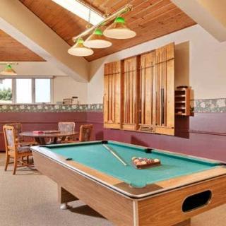 A cozy game room featuring a pool table under warm lighting, with wooden accents and additional seating in the background.