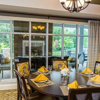 A well-decorated dining room with a round table set with yellow napkins and large windows overlooking a patio.