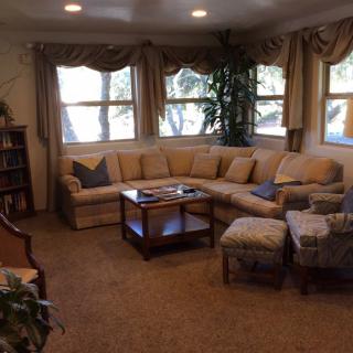 A cozy living room with a sectional sofa, coffee table, and multiple windows with curtains.