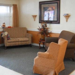 A cozy living room with various chairs, a painting on the wall, and a window letting in natural light.