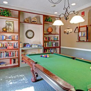 A cozy game room featuring a green pool table and bookshelves, perfect for relaxation and entertainment.