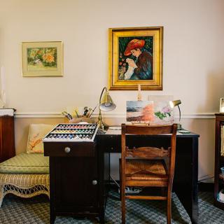 A cozy home office with a wooden desk and a classic chair, enhanced by artwork hanging on the wall.