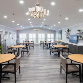 A modern dining area with elegantly arranged tables and chairs, featuring a central chandelier and bright lighting.