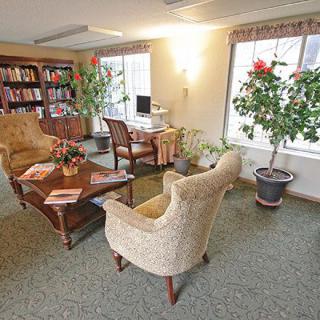A cozy reading area with armchairs, a table, bookshelves, and indoor plants.