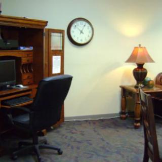 A tidy office setup with a computer desk, chair, and a lamp on a side table.