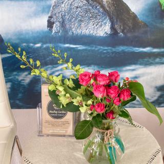 A beautiful floral arrangement featuring vibrant pink roses and delicate greenery, set against a serene ocean backdrop.