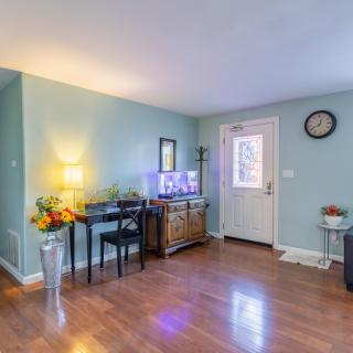 A cozy living room with hardwood flooring, featuring a table with a lamp and flowers, a fish tank, and a clock on the wall.