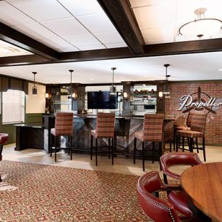 A cozy bar lounge with comfortable seating and a television, featuring modern lighting and a patterned carpet.