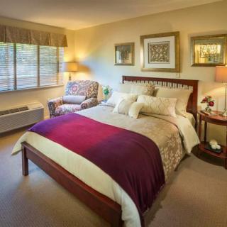 Cozy bedroom with a neatly made bed, armchair, and soft lighting.