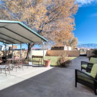 A backyard patio with outdoor seating under a canopy, surrounded by trees and set against a clear blue sky.