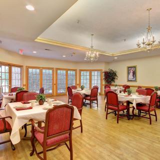 A spacious dining area with elegantly set tables and red chairs, featuring chandeliers and large windows.