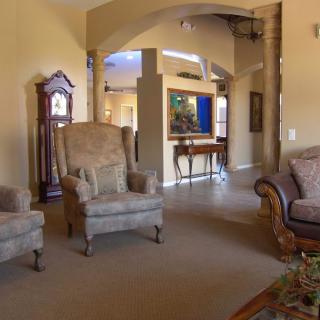 A cozy living room featuring elegant armchairs, a classic sofa, and a grandfather clock, with an open archway leading to another area.