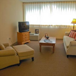 A cozy living room featuring a sofa, a small table, and a television, with natural light streaming through the curtains.
