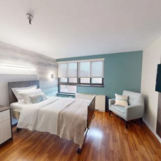 A modern and minimalist bedroom with a comfortable bed, an armchair, and large windows providing natural light.