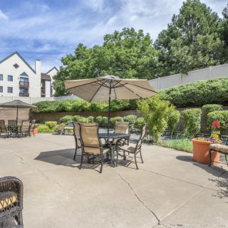 A sunny patio area with tables and chairs under umbrellas, surrounded by lush greenery.