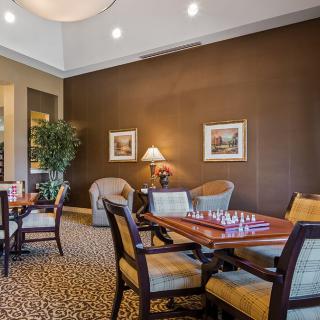 A cozy lounge area featuring tables with chess boards, comfortable seating, art on the walls, and ambient lighting.