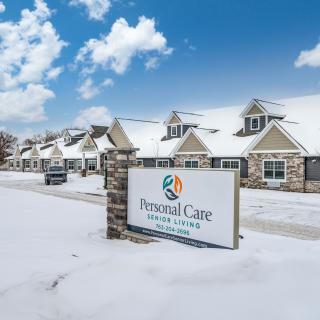 A snow-covered building with a sign reading 'Personal Care' under a cloudy sky.