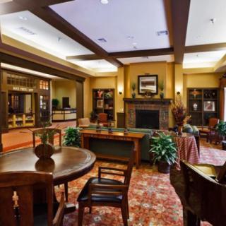 A cozy lounge area with a fireplace, surrounded by tables and chairs, adorned with plants and warm lighting.