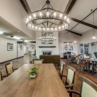 A spacious dining room with a large wooden table, elegant chandeliers, and modern decor.