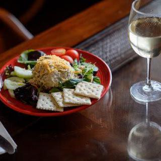 A gourmet meal with a fresh salad, cheese ball, crackers, and a glass of white wine.