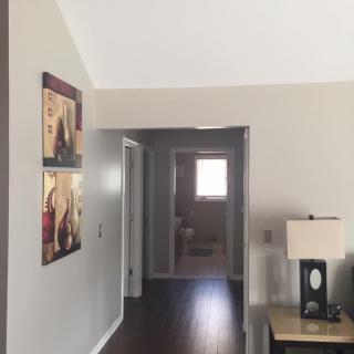 A view of a hallway from a living room, featuring wall art and a table lamp.