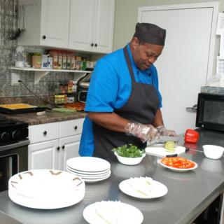 A chef in a blue shirt and black apron prepares vegetables in a kitchen setting.