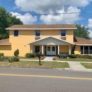 A two-story yellow house with a front porch and driveway on a sunny day.