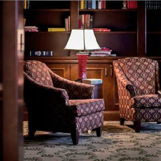 A cozy reading area with patterned armchairs and a lamp in a library setting.
