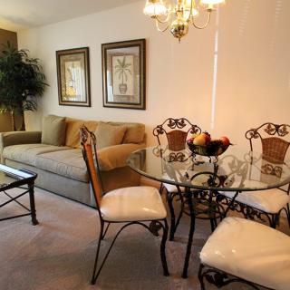 A cozy living room with a dining area featuring a glass table and upholstered chairs, complemented by elegant decor and wall art.