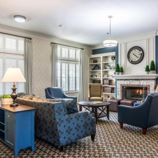 A cozy living room with comfortable seating around a fireplace, featuring elegant decor and a bookshelf.
