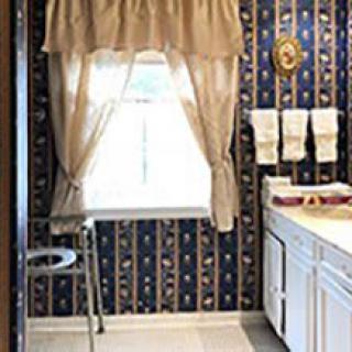 A retro kitchen featuring patterned wallpaper, a curtained window, and white cabinets.