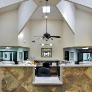 A spacious office reception area with a high ceiling, ceiling fan, and a central desk surrounded by marble flooring.