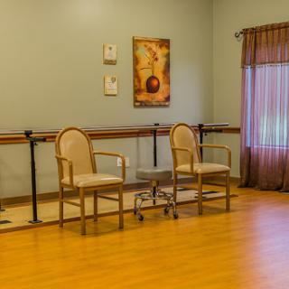 A spacious dance studio featuring two chairs, wooden flooring, and soft natural lighting.