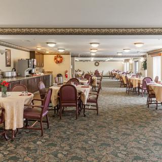 A spacious dining area with neatly arranged tables and chairs, featuring a buffet station and carpeted flooring.