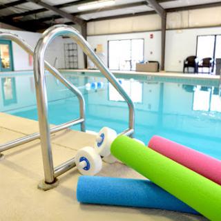 An inviting indoor swimming pool with colorful pool noodles and safety handrails.