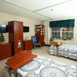 A hospital room featuring two beds, a window, and medical furniture.
