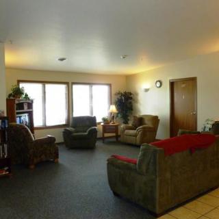 A cozy living room with multiple sofas and chairs arranged around a television, featuring a large window and soft lighting.