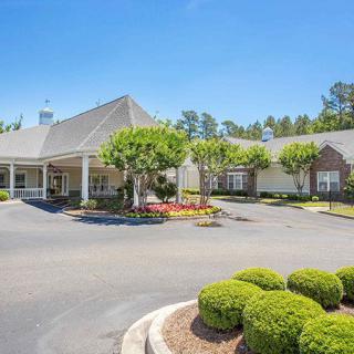 A sunny view of a building surrounded by greenery and a driveway.