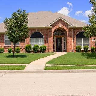 A suburban brick house with a well-maintained lawn and trees.