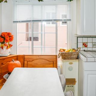 A cozy kitchen nook with a table, decorated with pumpkins and flowers, next to a window with blinds.