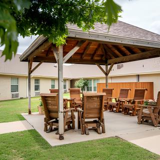 A cozy outdoor patio area with wooden gazebo and seating, set on a lush green lawn.