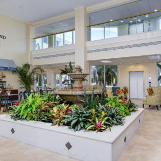 A spacious lobby featuring a central fountain surrounded by lush greenery and seating areas.