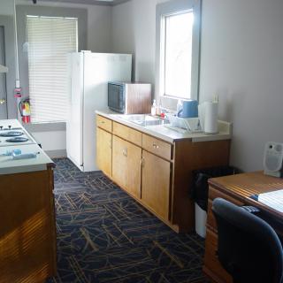A modest kitchen area with wooden cabinets, a refrigerator, and a small desk with a chair near the window.