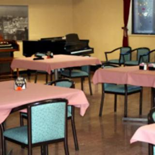 An empty dining area with neatly arranged tables and chairs, featuring a piano in the corner.