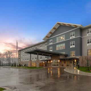 A modern hotel entrance illuminated at dusk, showcasing contemporary architecture against a rainy landscape.