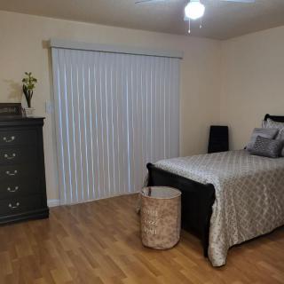 A minimalistic bedroom with neutral colors featuring a bed, dresser, wooden floor, and vertical blinds.