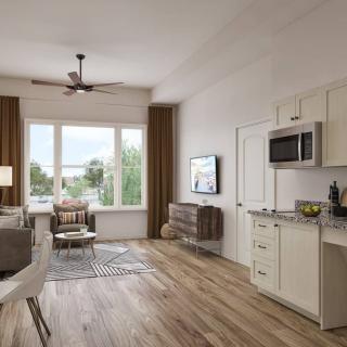 A modern apartment interior with a combined living room and kitchen, featuring wood flooring and ample natural light.