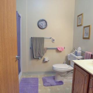 A neatly arranged bathroom with a clock on the wall, purple rugs, and towels.