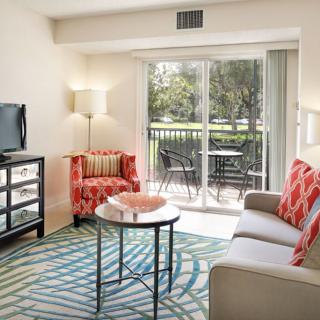 A cozy living room with a sofa, armchair, and coffee table facing a television, featuring patio doors that open to an outdoor space.