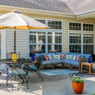 A cozy outdoor patio area featuring a sectional sofa with colorful cushions, a dining table with an umbrella, and a potted plant.